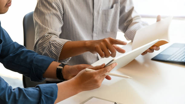 istock Cropped image of architect team holding a computer tablet and notebook and planning/talking about their project while sitting at the modern meeting table with comfortable office as background. 1211921930