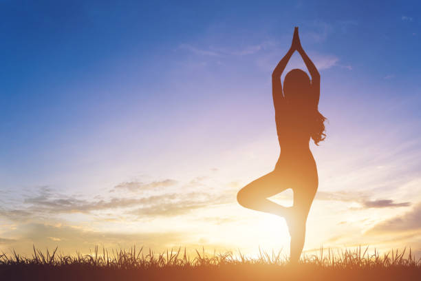 istock Young woman silhouette practicing yoga on sunrise sky background. 1211926321