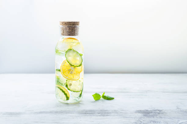 Detox Sassy water with lemon, cucumber and mint. A glass bottle of clean, cool and fresh drink stands on a white wooden table with a cotton natural napkin. Beautiful diet, Still life with copy space.