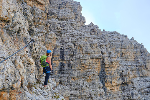 Woman on via ferrata Cesare Piazzetta, looking ahead at an exposed section with impressive rock walls around it. Active holiday in Sella group, Dolomites mountains, Italy.
