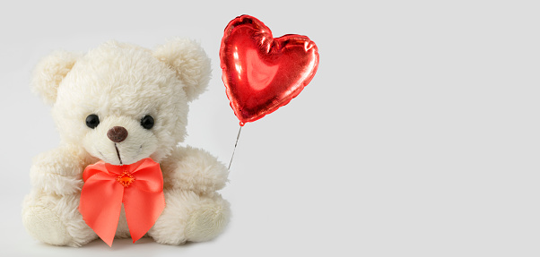Cute teddy bear holds a heart ball. Valentine with a bear.