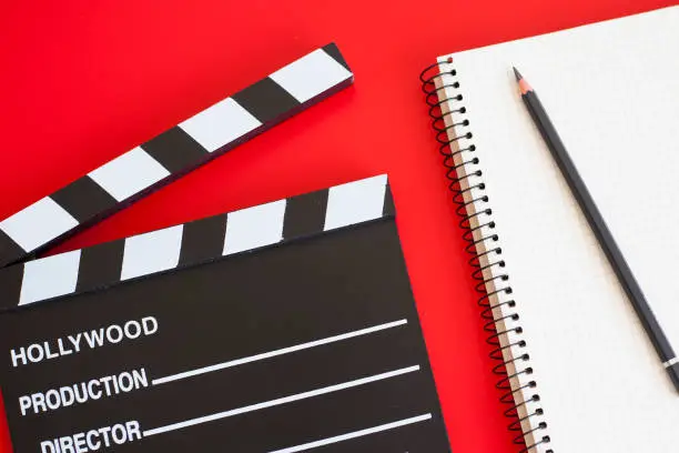 Photo of film clapper and pen notepad on red background