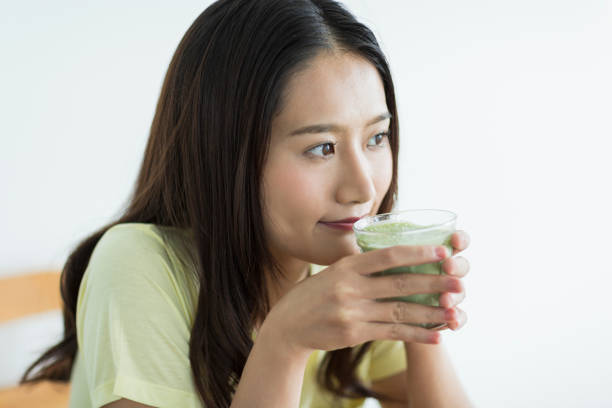 giovane donna che beve un frullato verde - healthy eating juice vegetable juice vegetable foto e immagini stock