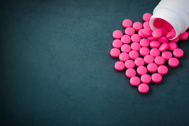 las píldoras rosas se dispersan de un frasco sobre un fondo gris. - pink pill fotografías e imágenes de stock