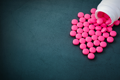Pink pills are scattered from a jar on a gray background.