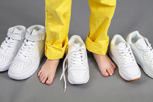 Barefoot on the background of shoes. Feet in a pile of shoes. Children's foot on the background of sneakers. Foot and shoes