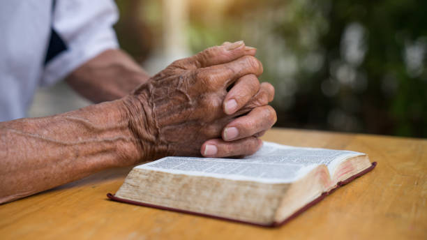 istock Old man reading her bible while sitting outside 1211950782