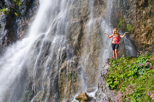 Woman posing in front of Dalfazer waterfall with her arms spread out as a Libra scale sign.