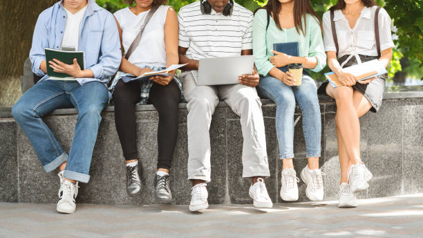 istock Diverce university students sitting outdoors with laptop and workbooks, studying together 1211952330