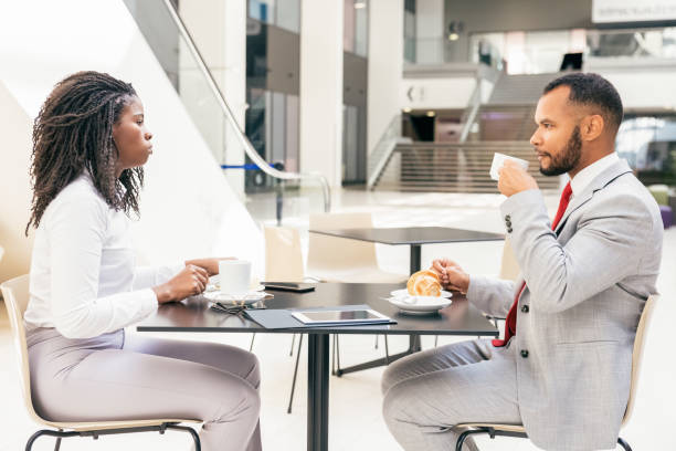 Diverse partners or colleagues meeting over cup of coffee. Side of business man and woman sitting at table in cafe, drinking coffee and talking. Business meeting or coffee hour concept