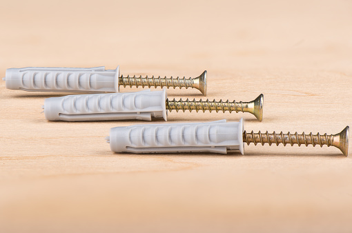 Metal screws and plastic dowels on a wooden background. Close up. Copy space.