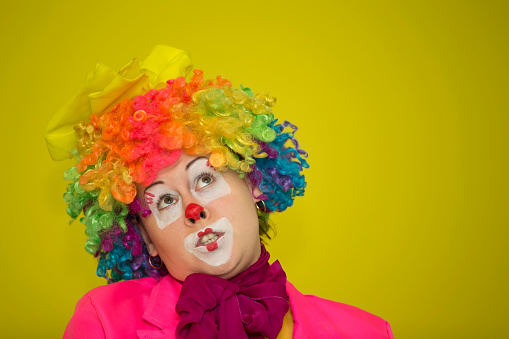 Merry clown. Shows a grimace.Woman clown in a wig on a yellow background.
