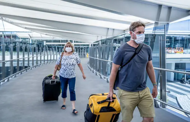 Photo of Senior woman and adult son wearing face mask at airport in fear of coronavirus and travel ban and international trips cancellations for disease control and prevention of COVID-19 outbreak pandemic.
