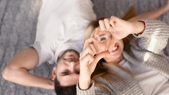 Young man and his girlfriend making heart with her hands indoors, top view. Selective focus