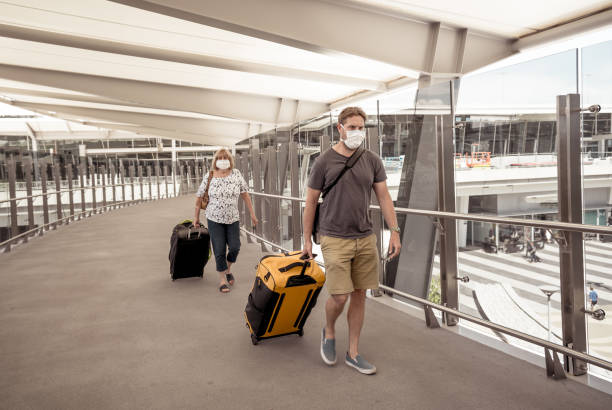 Senior woman and adult son wearing face mask at airport in fear of coronavirus and travel ban and international trips cancellations for disease control and prevention of COVID-19 outbreak pandemic. mujer mayor y hijo adulto que lleva máscara facial en el aeropuerto por temor al coronavirus y la prohibición de viajar y cancelaciones de viajes internacionales para el control de enfermedades y la prevención de la pandemia de brote covid-19.