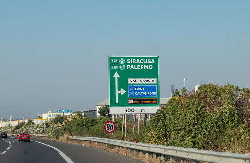 Siracusa in Sicily, Italy. Vehicle registration plates are visible in the background, as well as company names and logos.