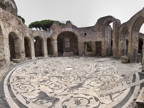 Ostia Antica, Italy - July 09, 2019: Immersive panoramic view of the circular hall of the seven wise thermal baths in archaeological excavation of Ostia Antica, with the beautiful polychrome mosaic heritage of Roman art. Rome,  Italy