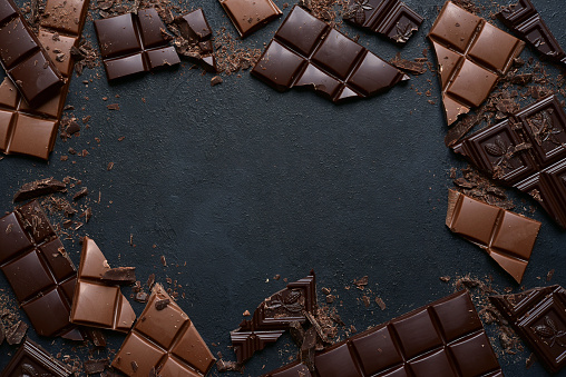 Slices of dark and milk chocolate on a black slate, stone or concrete background. Top view with copy space.