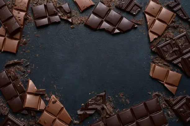 Slices of dark and milk chocolate on a black slate, stone or concrete background. Top view with copy space.