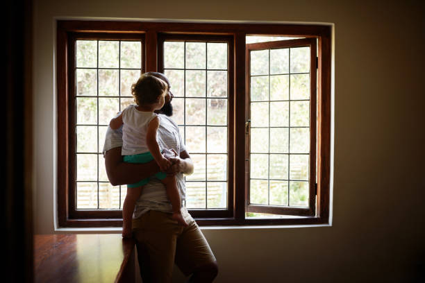Shot of a young man looking out of the window with his adorable child in their new home