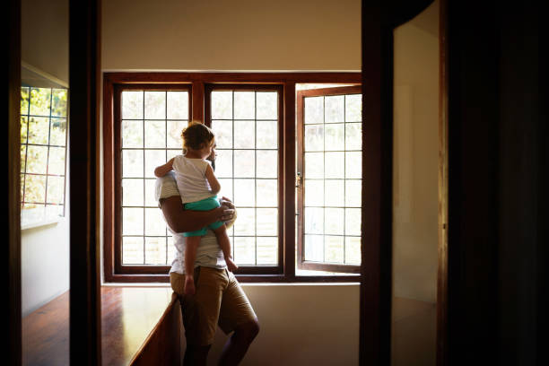 Shot of a young man looking out of the window with his adorable child in their new home