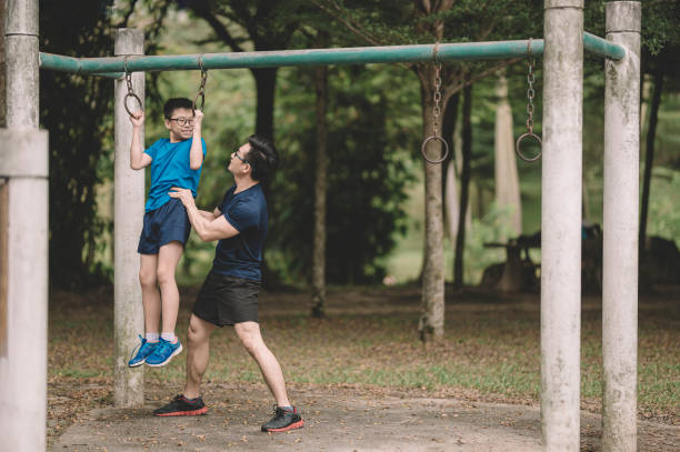 アジアの中国人の父アスリートが、夕方のリフトアップバーで公共公園で12歳の息子を訓練する - 12 13 years ストックフォトと画像