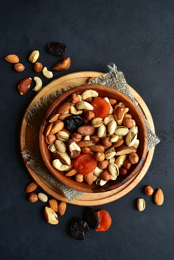 Wooden bowl with assortment of dried fruits and nuts on a black slate, stone or concrete background. Top view with copy space.