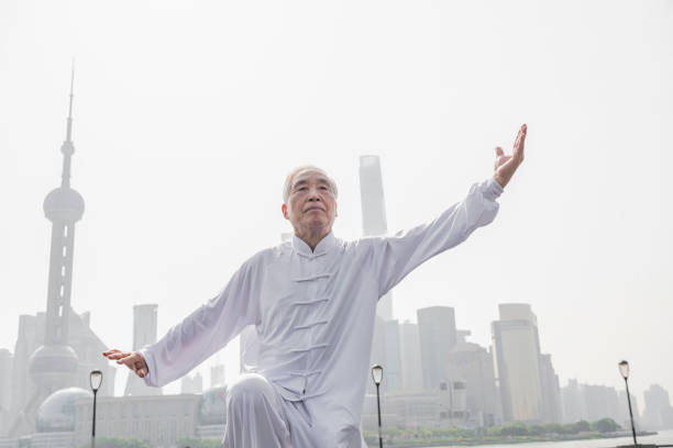 Close-up of poised senior Chinese man doing Tai Chi on The Bund with Pudong landmarks across the river in the background.