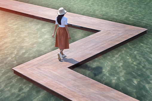 woman in dress walks on wooden bridge laying on the sea beach