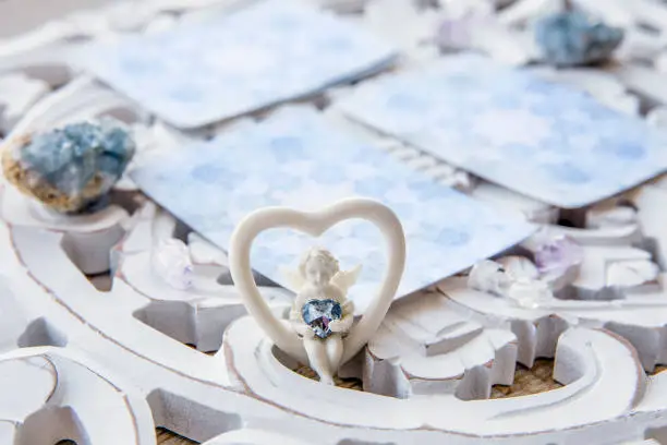 Photo of Deck with divination homemade Angel cards on bright white table, surrounded with semi precious stones crystals. Selective focus on cute angel figurine.
