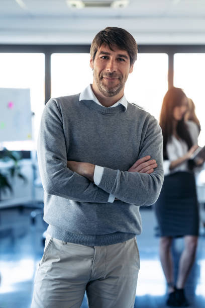 istock Handsome businessman is looking at camera while his colleagues are working on coworking place. 1211967905