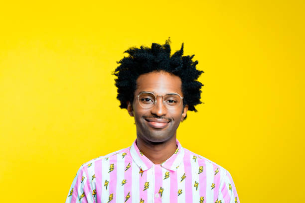 Friendly young man wearing vintage shirt, portrait on yellow background Portrait of happy afro american young man with dreadlocks wearing vintage shirt with lightning pattern, smiling at camera. Studio shot on yellow background. smirking stock pictures, royalty-free photos & images