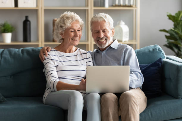 istock Smiling elderly husband and wife rest on sofa using laptop 1211971809