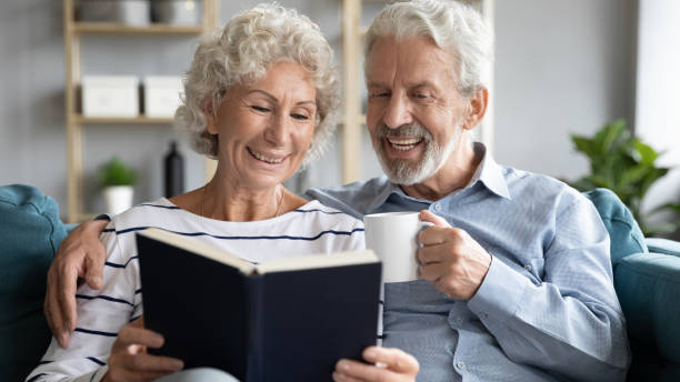 istock Smiling old couple relax at home reading together 1211971820