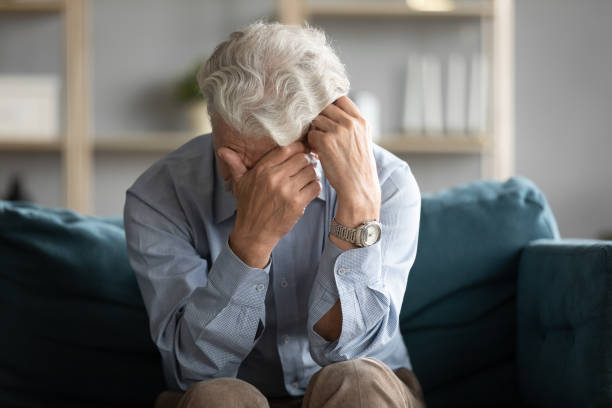 unglücklicher alter mann sitzt auf der couch weinende sehnsucht - senior male sad stock-fotos und bilder