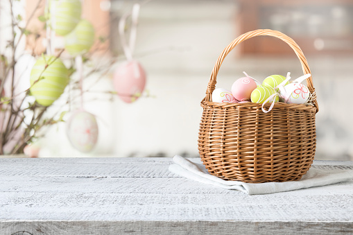 Wicker basket with easter colorful eggs on kitchen white wooden table. Spring easter composition. Space for text or design.