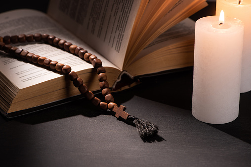 holy bible with rosary on black dark background with burning candles