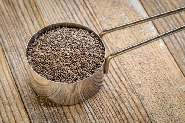 chia seeds in metal measuring scoop against grunge wood background, healthy superfood concept