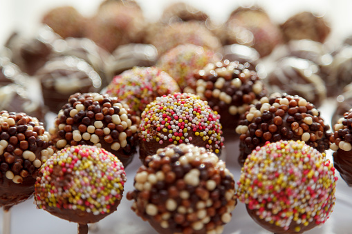 Close up of a collection of delicious chocolate lollipops with various colourful sprinckles on top, with the nack rows out of focus