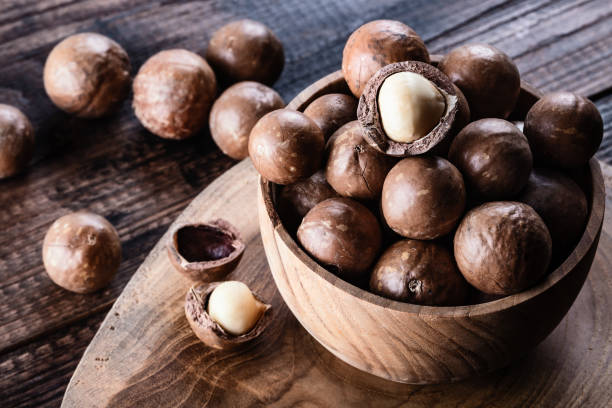istock Organic ripe whole Macadamia nuts in bowl on old wooden rustic table 1211981090