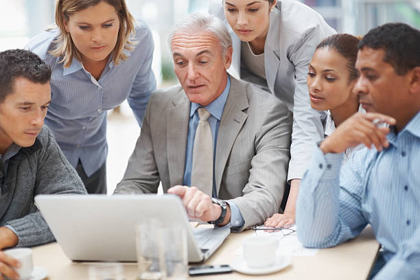 istock Businessman points at laptop screen while discussing with team 121198419