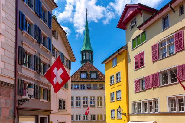 Swiss flag waving, church and colorful facades of houses in Old Town of Zurich, the largest city in Switzerland in sunny day.