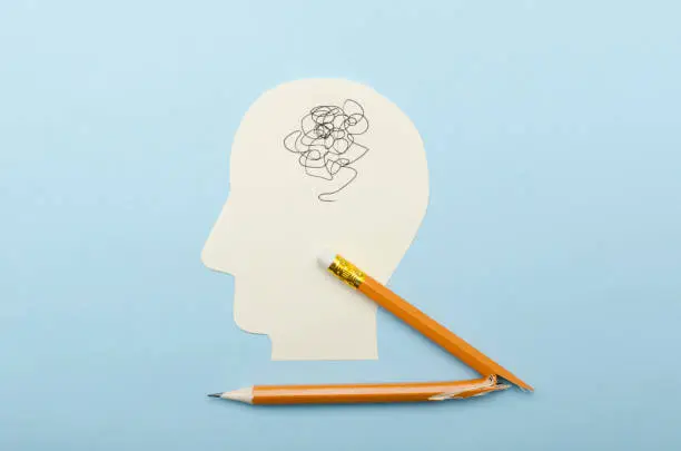 Photo of Concept of emotional catatonia and mental block.Top view of paper head as a symbol of mess with head and broken pencil on the blue background