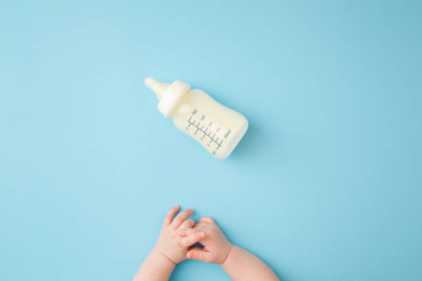 Infant hands and bottle of milk on light blue table background. Feeding time. Pastel color. Closeup. Point of view shot. Top down view. Infant hands and bottle of milk on light blue table background. Feeding time. Pastel color. Closeup. Point of view shot. Top down view. babyhood stock pictures, royalty-free photos & images