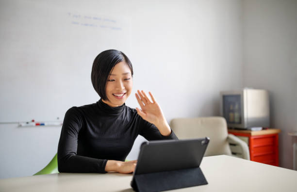 Female professional making a video call in office Businesswoman working in office, doing a video call with digital tablet. Female professional working in office and making a video call. waving gesture stock pictures, royalty-free photos & images