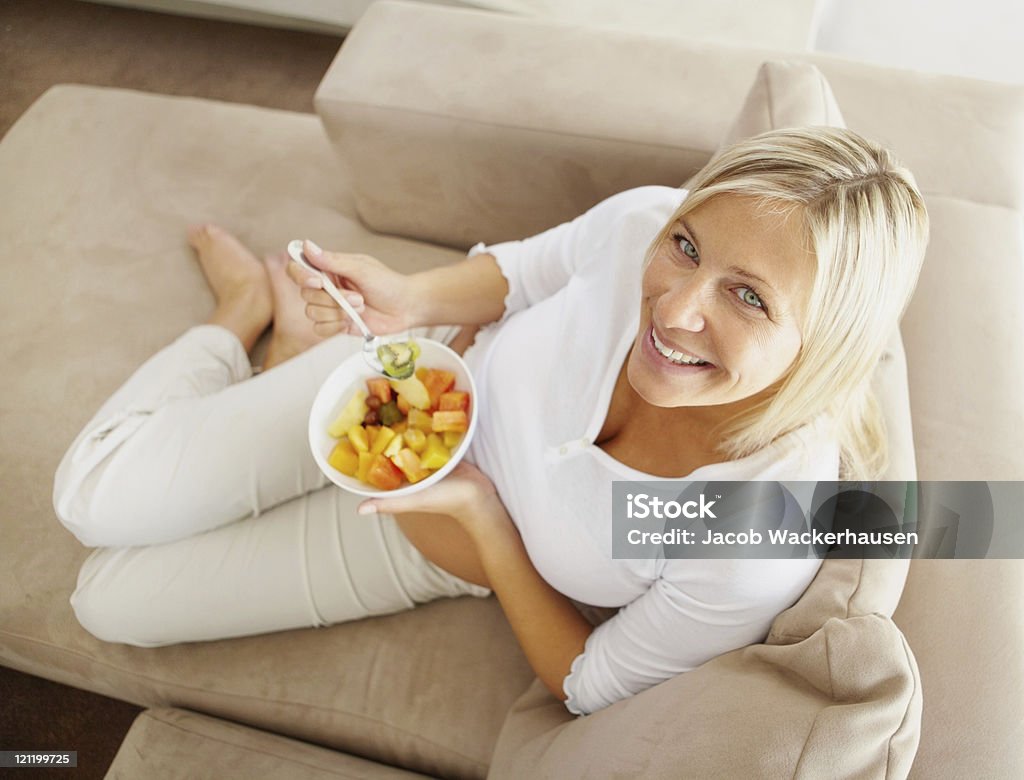 Vista dall'alto di una donna matura rilassante sul divano mangiando - Foto stock royalty-free di Mangiare