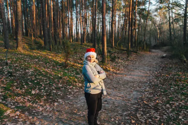 December 1, 2018 - Kampinos, Poland:  pretty blond woman in Santa hat standing and smiling in a beautiful pine forest on a cold autumn day