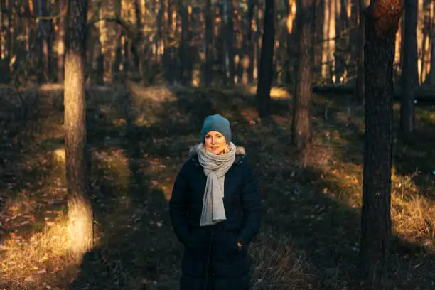 December 1, 2018 - Kampinos, Poland: attractive young woman standing in the shadow in a pine tree forest being cold, serious, looking at camera