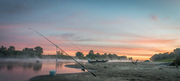 Foggy sunrise landscape. Mature man fishing on a lake, standing in the water. 