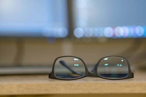 istock Closeup of protective glasses on an empty desk with blurred computer screen on background. 1212001189
